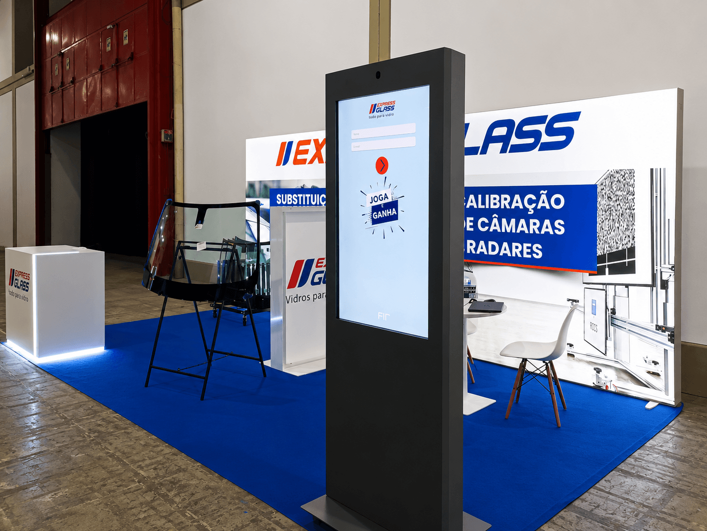 Estande da Express Glass com quiosque digital, para-brisa em suporte e painéis sobre carpete azul.